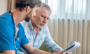 Lekarz w niebieskim fartuchu omawia wyniki badań z pacjentem. Mężczyzna z siwą brodą uważnie słucha, analizując dokumenty dotyczące biopsji prostaty.