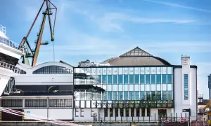 Nowoczesny budynek Muzeum Emigracji z przeszkloną fasadą, gdzie mieści się restauracja, na tle portowego dźwigu.