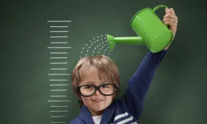 Niño con gafas riega su cabeza con una regadera verde, frente a una tabla de crecimiento que marca el percentil 10.