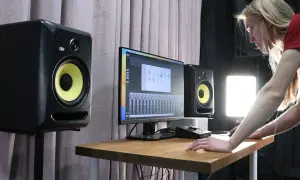 Młoda kobieta pracuje w studiu nagraniowym, otoczona monitorami studyjnymi KRK. Na biurku stoi komputer z programem do produkcji muzyki.