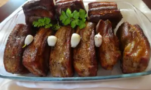 Pyszne żeberka w miodzie, pieczone z czosnkiem i natką pietruszki, prezentują się apetycznie na szklanej tacy.