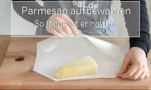 Ein Stück Parmesan wird auf Backpapier auf einem Holzbrett gelegt.