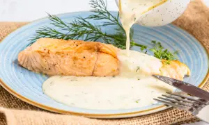 Ein goldbraunes Lachsfilet wird mit einer cremigen, Kräuter-haltigen Sauce übergossen. Perfekte Sauce zu gebratenem Lachs, garniert mit Dill.