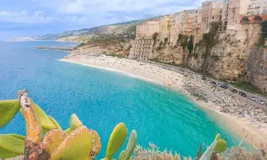 Vue panoramique de la plage de Tropea, Calabre, avec ses eaux turquoise, ses falaises et ses maisons colorées perchées.