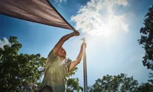 Man sätter upp ett solsegel mot en klarblå himmel med solens strålar som lyser.
