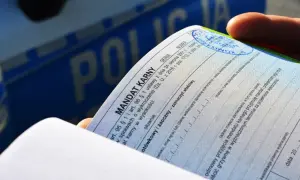 Dłoń trzyma mandat karny, dokument potwierdzający popełnienie wykroczenia. W tle widoczny napis "POLICJA".
