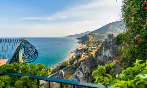 Balkonblick auf Siziliens Küste: Türkises Meer, felsige Hänge & blühende Pflanzen. Perfekt für Sizilien Urlaub Tipps!