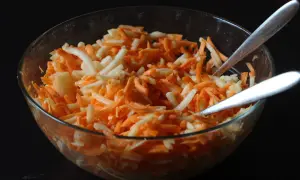 Schüssel mit geriebenen Karotten und Äpfeln, bereit für ein leckeres karottensalat rezept. Zwei Löffel warten darauf, den Salat zu servieren.