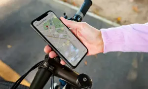 Dłoń trzyma smartfon z mapą, wskazującą trasę rowerową. Telefon pełni rolę licznika na rower, pokazując drogę do celu.
