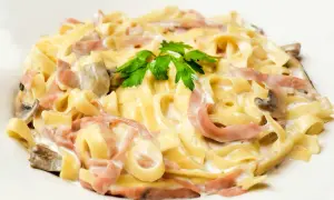 Makaron tagliatelle z szynką, pieczarkami i kremowym sosem, udekorowany natką pietruszki.