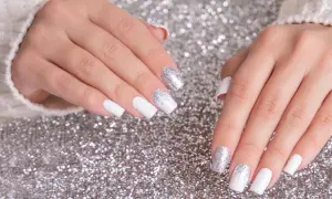 Dłonie z białym french manicure i brokatem na paznokciach, na tle srebrnego brokatu.