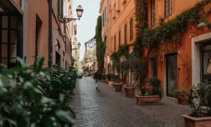 Eine Person geht durch eine schmale Gasse in Rom, gesäumt von orangefarbenen Gebäuden und Pflanzen. Ein perfekter Ort für Rom Geheimtipps.