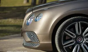 Detaljbild av en lyxig, brun Bentley till salu. Framhjulet och strålkastaren syns tydligt.