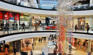 Bunte Papierkraniche schmücken ein Einkaufszentrum in Prag. Menschen bummeln durch die Gänge, vorbei an Geschäften und einer roten Sportwagen-Auslage.