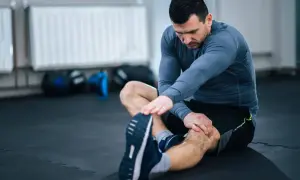 Mężczyzna wykonuje ćwiczenia rozciągające nogi na siłowni, siedząc na macie.