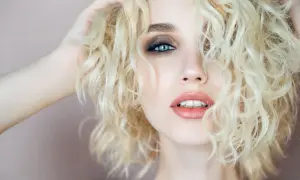 Capelli biondi e ricci, luminosi come la camomilla, incorniciano un volto con occhi azzurri e labbra sensuali.