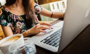 Ragazza con laptop e caffè, mentre cerca la differenza ferie e permessi.