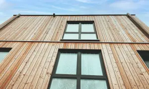 Moderne Holzfassaden Beispiele: Natürliche Holzverkleidung mit großen Fenstern unter blauem Himmel.