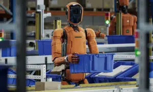 Pomarańczowy robot w magazynie przenosi niebieskie pudełko. To jest robot, który pracuje.