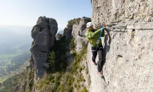 Un homme équipé pour la via ferrata progresse sur une paroi rocheuse, profitant d'un paysage spectaculaire.