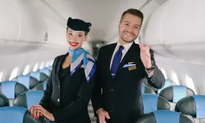 Uśmiechnięci steward i stewardessa w uniformach LOT. Spełniają wymagania, by zapewnić komfort podróży.