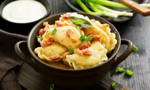 Pyszne pierogi z boczkiem i szczypiorkiem. Wiesz, ile gotować pierogi, by były idealne? Podane z kwaśną śmietaną.