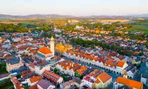 Luftaufnahme eines malerischen **Taus Tschechien** mit roten Dächern, einer Kirche und grünen Hügeln im Hintergrund.