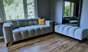Nowoczesna szara sofa i pufa, ozdobione żółtą poduszką. To meble od najlepszych producentów mebli tapicerowanych, idealne do stylowego salonu.