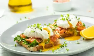 Dwa talerze z jajkami po benedyktyńsku na tostach z łososiem, sałatą i kiełkami. Płynne żółtko spływa po tostach.