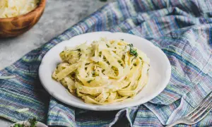 Pyszny sos do makaronu z parmezanem i ziołami na talerzu, obok miska z serem i widelcem.