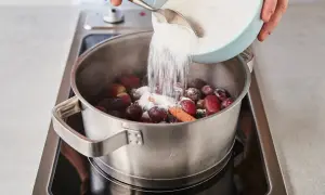 Zucker wird zu Trauben und Zimt in einem Topf gegeben, um köstliche Weintrauben Marmelade herzustellen.