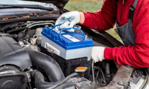 Persona con guantes blancos manipula una batería de coche azul y gris, lista para cargar batería coche.