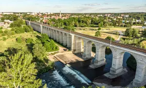 Kamienny wiadukt kolejowy nad rzeką, z miastem w tle. Bolesławiec atrakcje, które zachwycają.