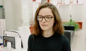 Młoda kobieta w okularach w panterkę, z lekko przekrzywionym wzrokiem, jakby szukała czegoś ukrytego.