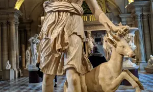 Statue de Diane chasseresse, qui est Artémis, tenant un cerf. L'œuvre est dans un musée, avec d'autres sculptures en arrière-plan.