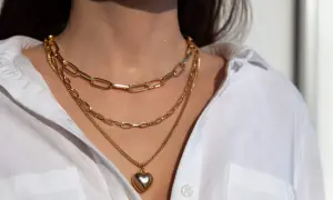 Tres collares dorados en capas, uno con un corazón, lucen perfectos con el escote de una camisa blanca.
