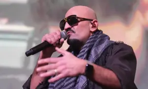 Ein bekannter Rapper mit Sonnenbrille und Schal spricht ins Mikrofon, während er gestikuliert.
