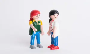 Twee Playmobil-poppetjes staan tegenover elkaar. De ene met rood haar en een groen vest, de ander met zwart haar en een wit shirt. Ze lijken te praten, alsof ze elkaar vertellen dat ik hoor niet bij mijn familie.