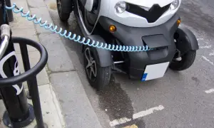 Biały, trójkołowy pojazd elektryczny podłączony do ładowarki. To pokazuje, jak zbudować samochód elektryczny, zaczynając od ładowania.