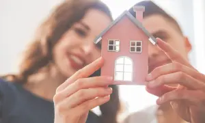 Coppia sorridente tiene in mano una casetta rosa, simbolo di un futuro progetto di comproprietà.