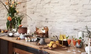 Vackert dukat långbord med påskbakelser, chokladtårta, drinkar och blommor.
