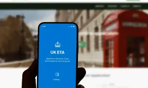 Telefon z aplikacją UK ETA, która pomaga sprawdzić, ile kosztuje wiza do Anglii. W tle londyńska budka telefoniczna.