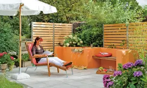 Entspannter Garten mit selbst gebautem Wasserfall. Eine Frau liest unter einem Sonnenschirm.