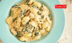 Gnocchi z kurczakiem w kremowym sosie ze szpinakiem i parmezanem na niebieskim talerzu.