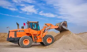 Pomarańczowa ładowarka Doosan zasypuje żwir na placu budowy pod błękitnym niebem.