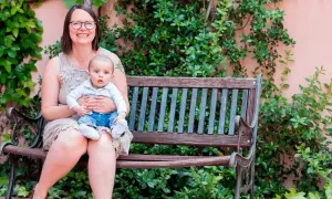 Madre sonriente abraza a su bebé en un banco. Un ejemplo de los hermosos testimonios de hijos nacidos por ovodonación.
