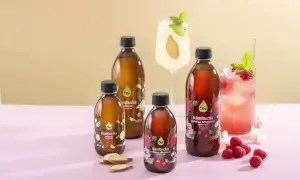 Butelki kombuchy, koktajle z owocami i imbirem na różowym tle.
