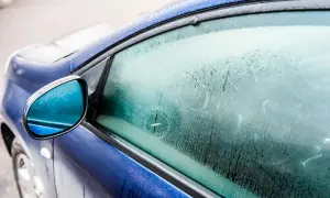 En blå bil med frost på sidorutan. Frågan "hur får man bort imma i bilen" är relevant när det är kallt ute.