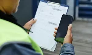 Pracownik w kamizelce odblaskowej trzyma telefon i dokumenty. Zastanawia się, czy warto złożyć skargę do PIP.