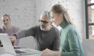 Uomo della generazione boomer spiega qualcosa su un laptop a una collega.